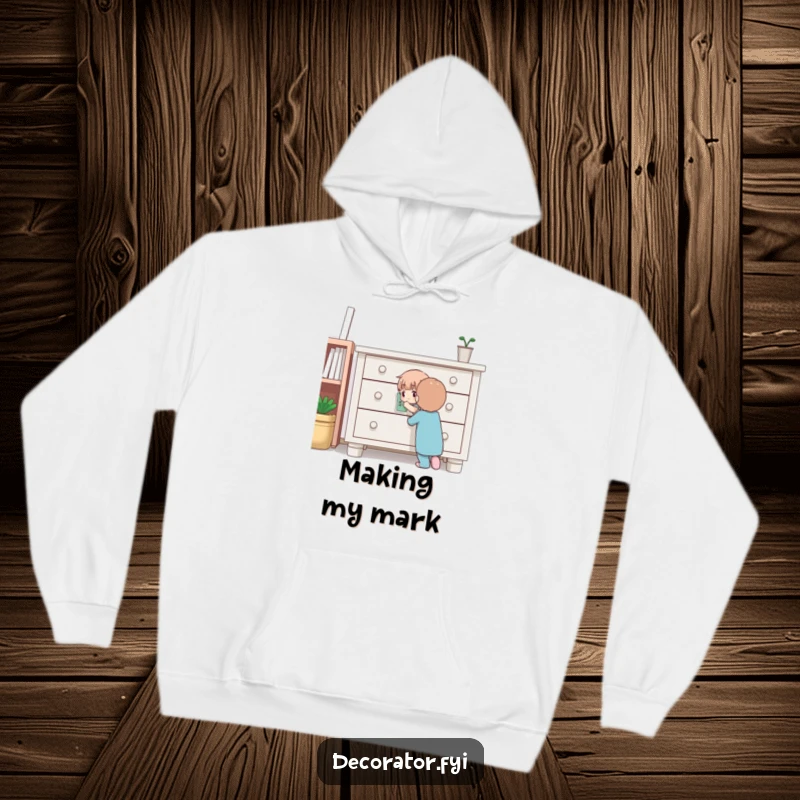 Funny hoodie depicting a determined character carefully applying a sticker to furniture, offering warmth and a humorous nod to DIY projects.